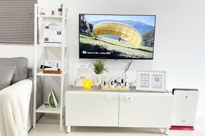 A modern living room with a flat-screen TV mounted on the wall, a white entertainment unit with decorative items, and a grey sofa. - Paradigm Residences 1 BR, above Paradigm Mall ,up to 5 Person (Johor Bahru)