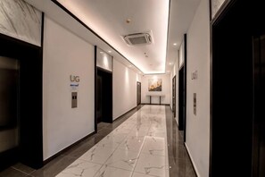 Pasillo de hotel con suelo de mármol, ascensores y un cartel en la pared.