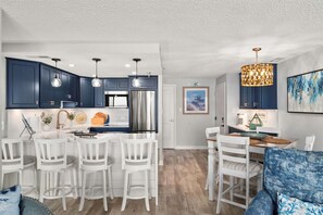 A modern kitchen with dark blue cabinets, a stainless steel refrigerator, and pendant lighting. - Sandy Square – Direct Oceanfront Condo 3BR • 2BA • Sleeps 11 (Ocean City)