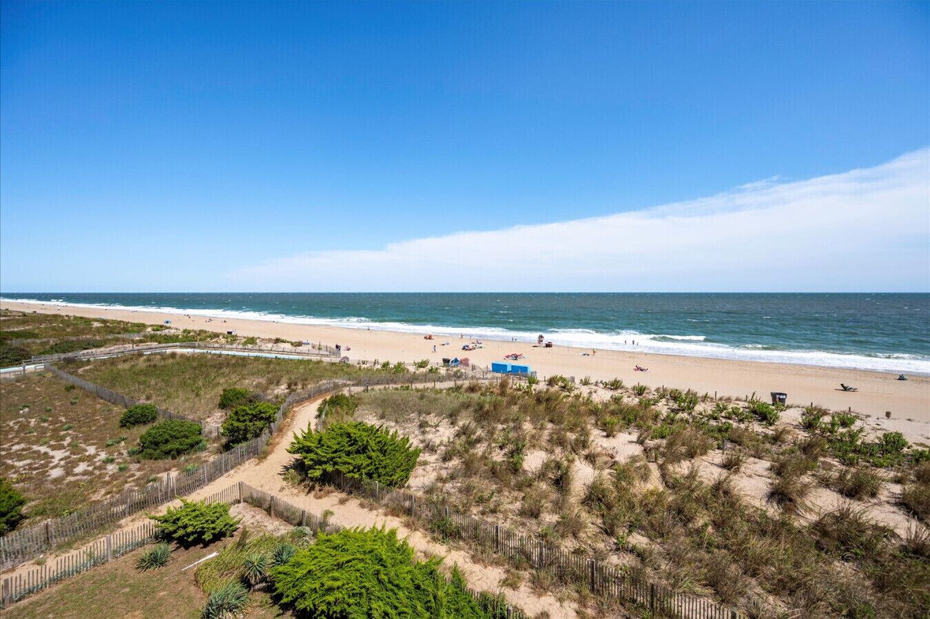 Une plage avec un sentier de sable, une clôture en bois et une vue dégagée sur l’océan.