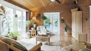 Een ruime woonkamer met een houten plafond, een plafondventilator, een groot raam en een bakstenen muur.
