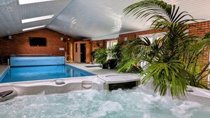 Ein Hallenbad mit Whirlpool, umgeben von Backsteinmauern und Pflanzen in Töpfen.