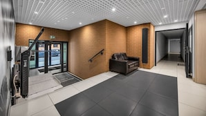 A modern lobby with a brick wall, a leather sofa, a staircase, and a reception desk. - Praga Apt - Parking, Terrace - by Rentujemy (Warszawa)