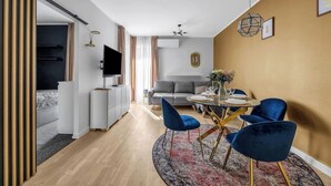 A modern living room with a dining area, featuring a sofa, a TV, and a dining table set for four. - Praga Apt - Parking, Terrace - by Rentujemy (Warszawa)
