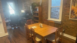 Een eetgedeelte met een houten tafel en stoelen, een bakstenen muur en een raam met uitzicht op bomen.