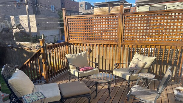Een houten terras met buitenmeubilair, waaronder een lounge stoel, fauteuils en een bijzettafeltje.