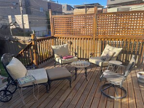 Terraza de madera con mobiliario exterior, incluyendo una tumbona, sillones y una mesita.