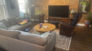 Een woonkamer met een bakstenen muur, een bank, een salontafel, een televisie en een stoel.