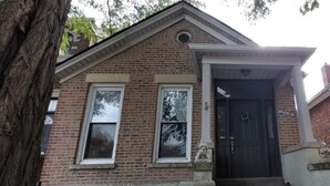 Een bakstenen gebouw met een zwarte deur, twee ramen en een stenen standbeeld.