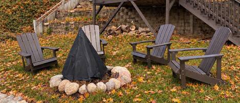 A deck with Adirondack chairs, a covered fire pit, and a stone border.