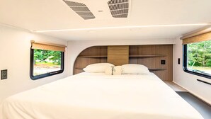 Une chambre moderne dans un véhicule récréatif, dotée d’un grand lit, de rangements intégrés et de grandes fenêtres.