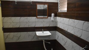 Un baño con un lavamanos blanco, paredes de baldosas marrón oscuro y un cubo de basura verde, además de un espejo.