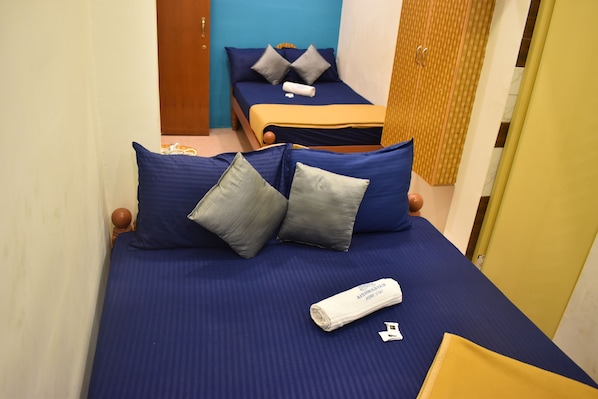 A hotel room with two beds, each with blue bedding and pillows, a wooden headboard, and a yellow accent wall. - Aishwaryam Home Stay (Madurai)