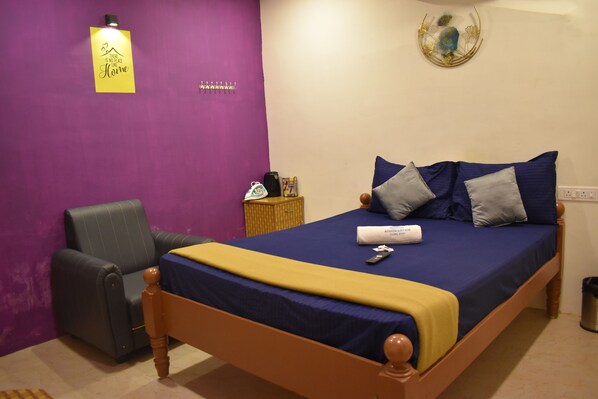 A bedroom with a bed, a chair, a nightstand, and a wall with a sign. - Aishwaryam Home Stay (Madurai)