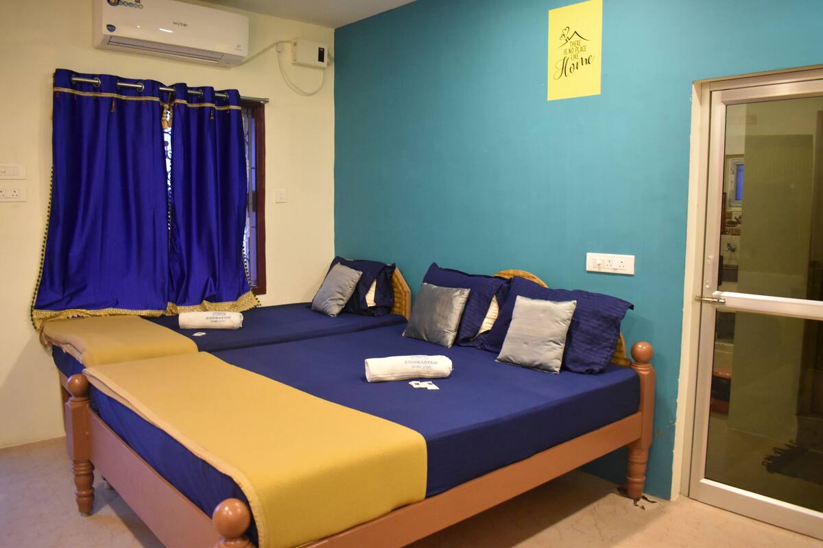 A double bed with blue and yellow bedding, a wooden headboard, and a window with blue curtains.