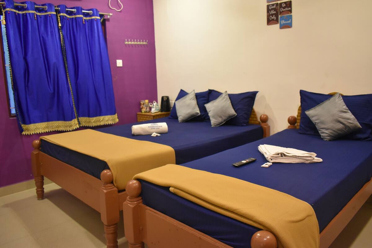 A room with two beds, each with a blue bedspread and pillows, a wooden headboard, and a yellow blanket.