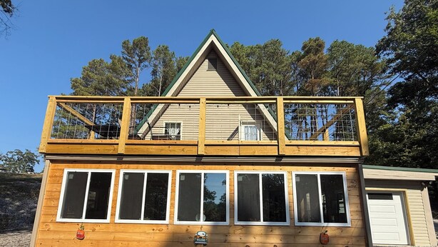 Een houten chalet met twee verdiepingen, een balkon op de bovenverdieping, grote ramen en een 'Welcome'-bord.
