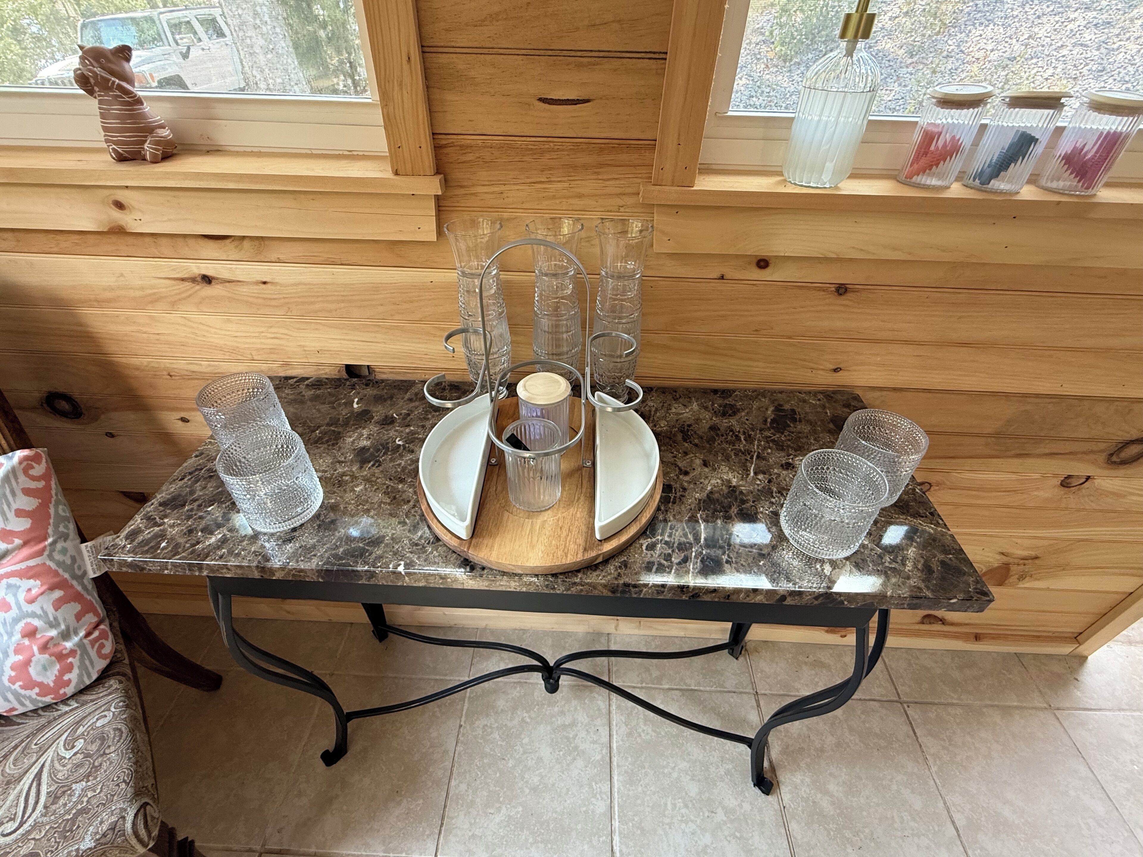 A wooden interior with a marble table, clear glassware, and a decorative bear figurine.