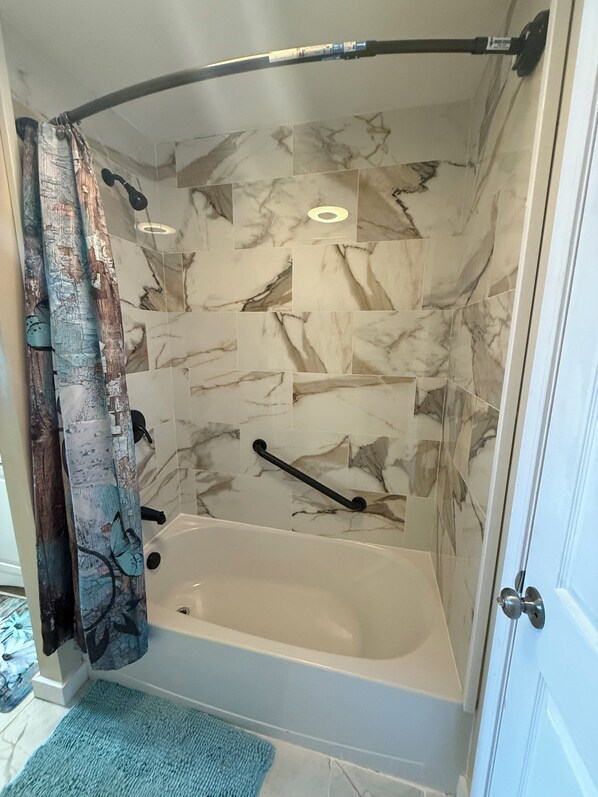 Une douche dotée d’un pommeau de douche incurvé, d’un flexible de douche et d’une baignoire équipée d’une barre d’appui.