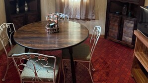 Un comedor con una mesa redonda, cuatro sillas, dos armarios de madera y una ventana con cortinas.