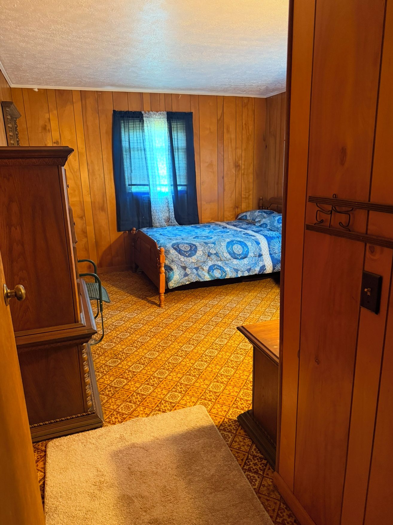 Une chambre avec des murs en bois, un lit recouvert d’une courtepointe à motifs, une armoire en bois et une petite table.