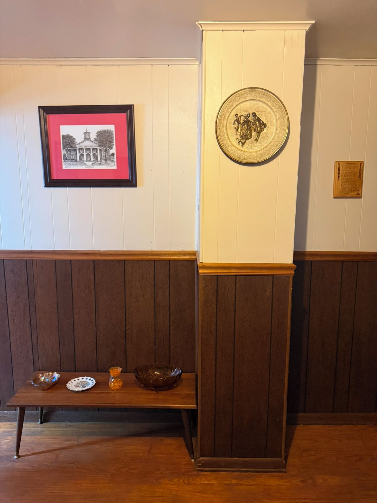 Una habitación con un banco de madera, un cuadro enmarco y un plato decorativo en la pared.