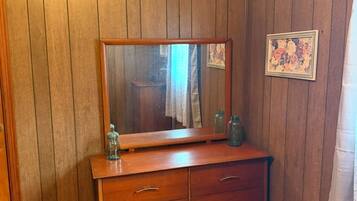 A room with wooden panel walls, a wooden dresser with drawers, a mirror, and a framed picture.