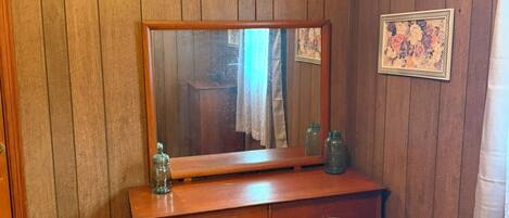 Une pièce aux murs recouverts de lambris en bois, une commode en bois avec des tiroirs, un miroir et un tableau encadré.