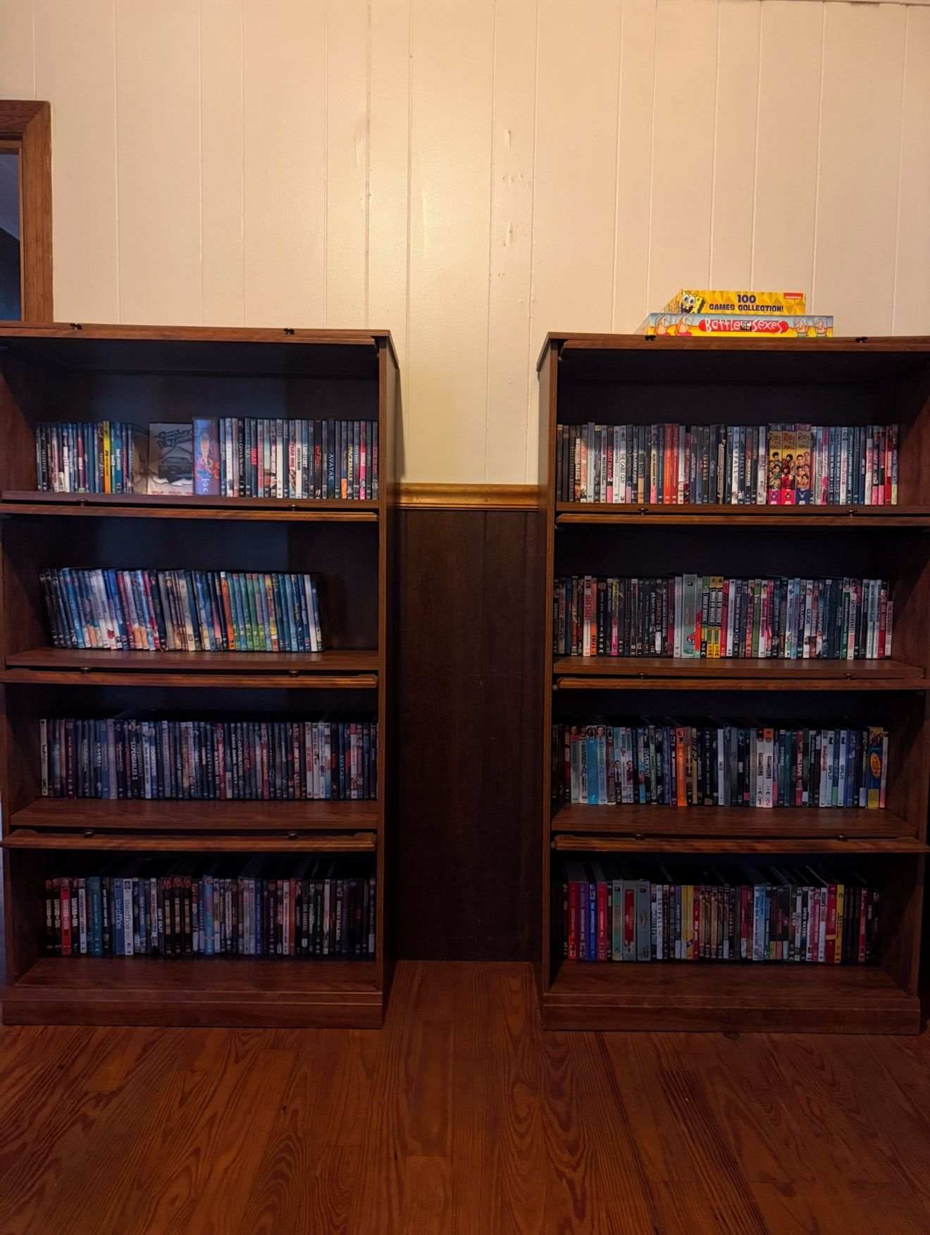 Deux étagères en bois, remplies de DVD, sont adossées à un mur blanc.