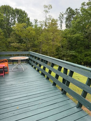 Une terrasse en bois avec une rambarde verte, une table et une chaise orange.