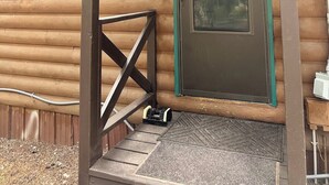 A log cabin with a green door, a porch with a bench, and string lights.