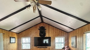 A cozy cabin-style room with a ceiling fan, a mounted television, and a large stuffed animal.