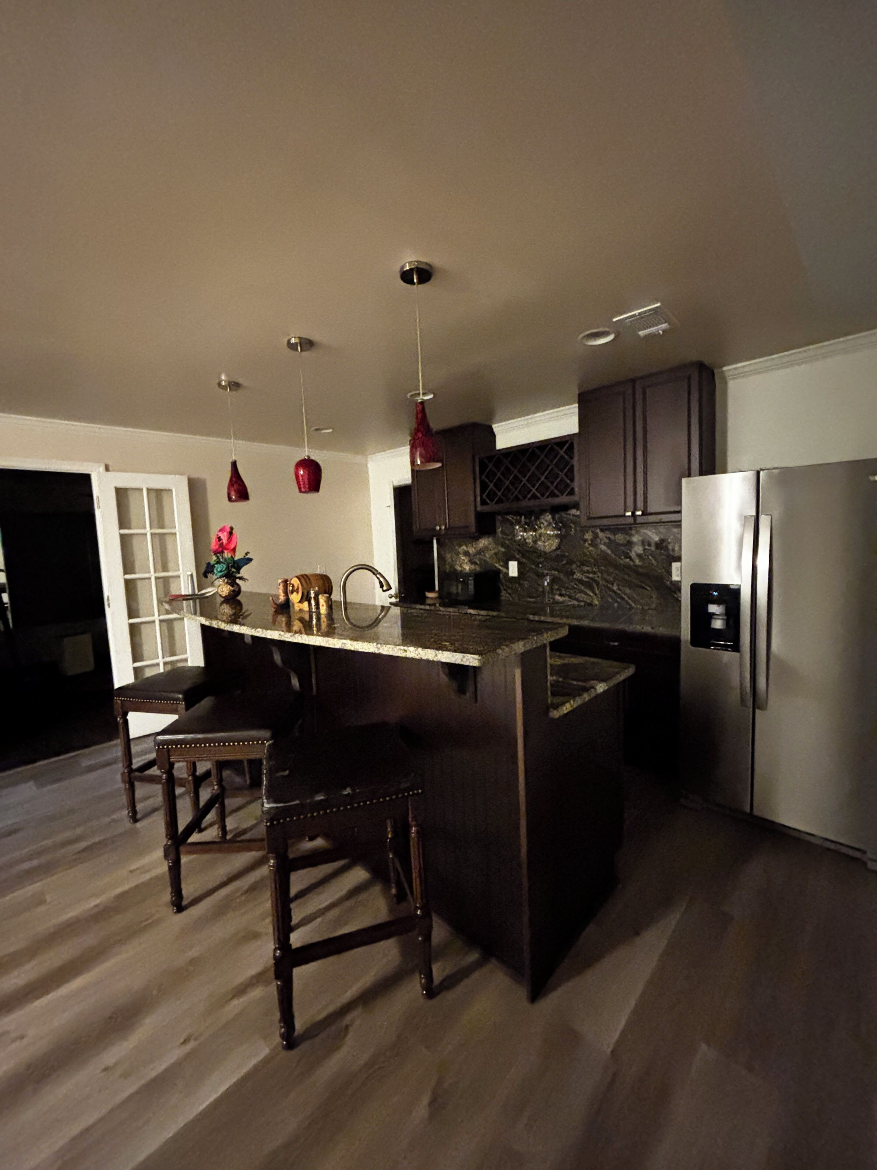 A modern kitchen with a central island, dark wooden bar stools, stainless steel appliances, and pendant lighting.