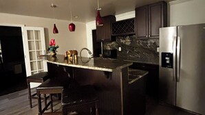 A modern kitchen with a central island, dark wooden bar stools, stainless steel appliances, and pendant lighting.