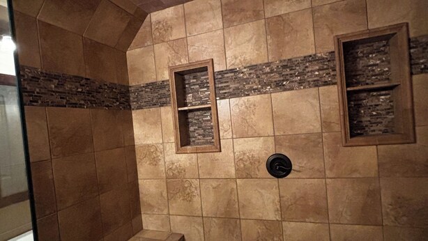 A tiled shower area with a bench, a showerhead, and two framed pictures on the wall.