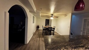 A kitchen with a granite countertop, a dining table with chairs, a ceiling fan, and a red pendant light.