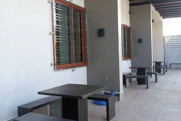 A covered outdoor area with tables and benches, a hose, and a wall-mounted speaker.