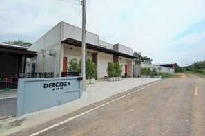 A modern building with a sign reading 'DEECOZY 41 43 43' and a paved road in front. - Deecozy (Hat Yai)