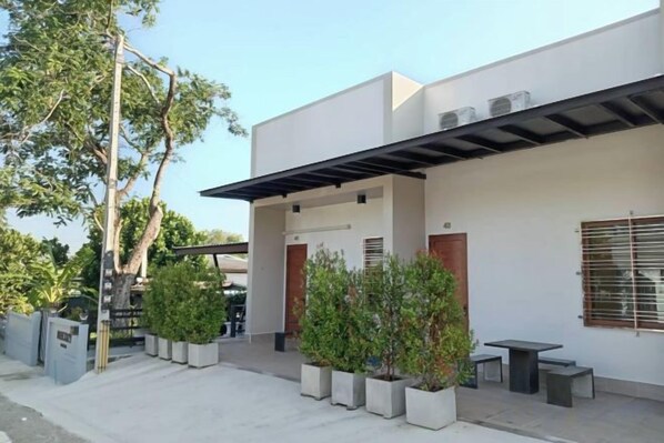 Un edificio moderno con un patio cubierto, plantas en macetas y una pequeña mesa.
