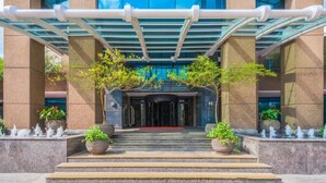 Una entrada moderna a un edificio con fachada de vidrio, zona de acceso cubierta y escalones que conducen a las puertas.