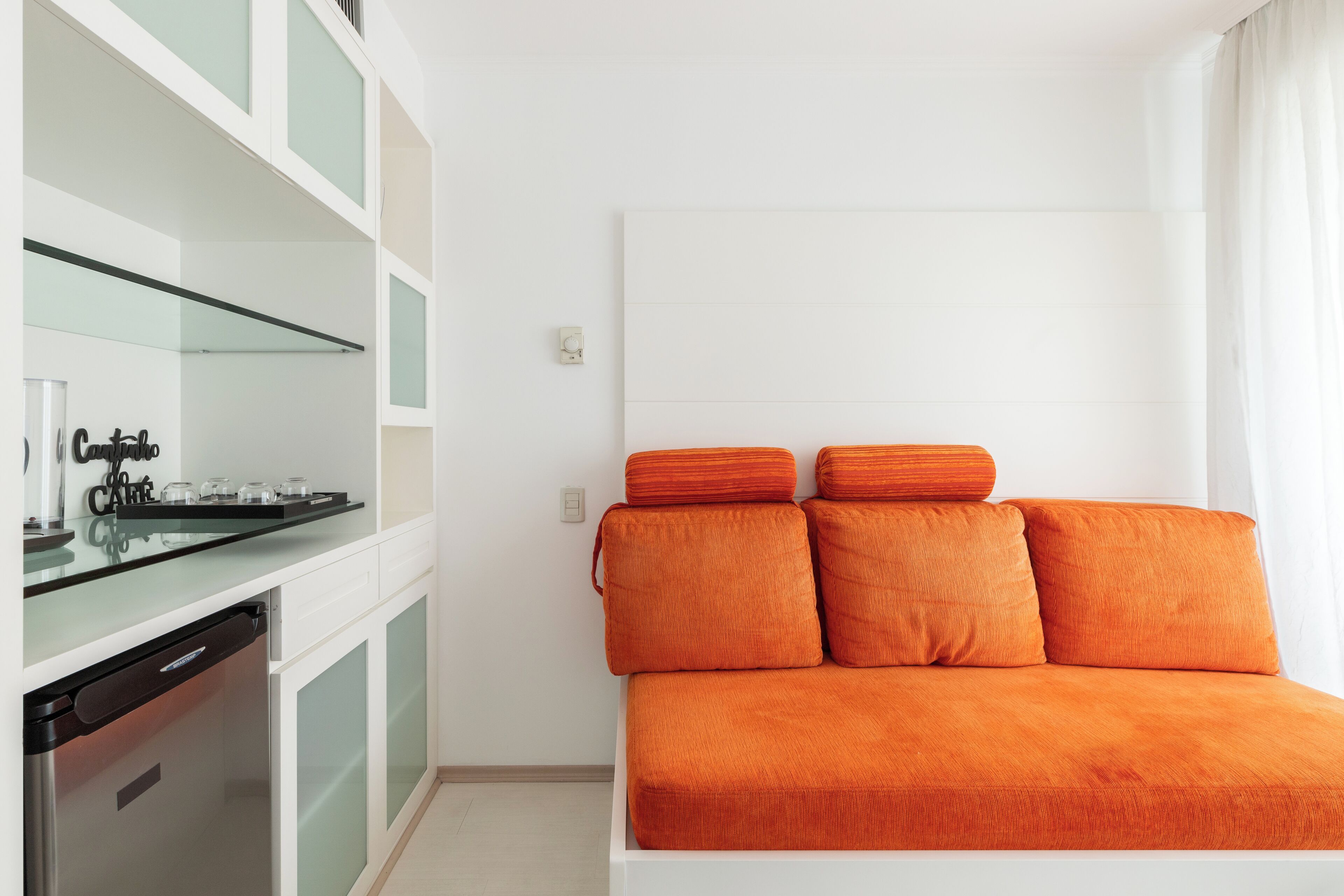 A modern room with a glass-top kitchen counter, a built-in dishwasher, and a large bed with orange bedding.