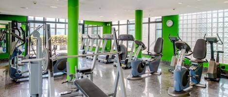 A gym with various exercise equipment, large windows, and green pillars.