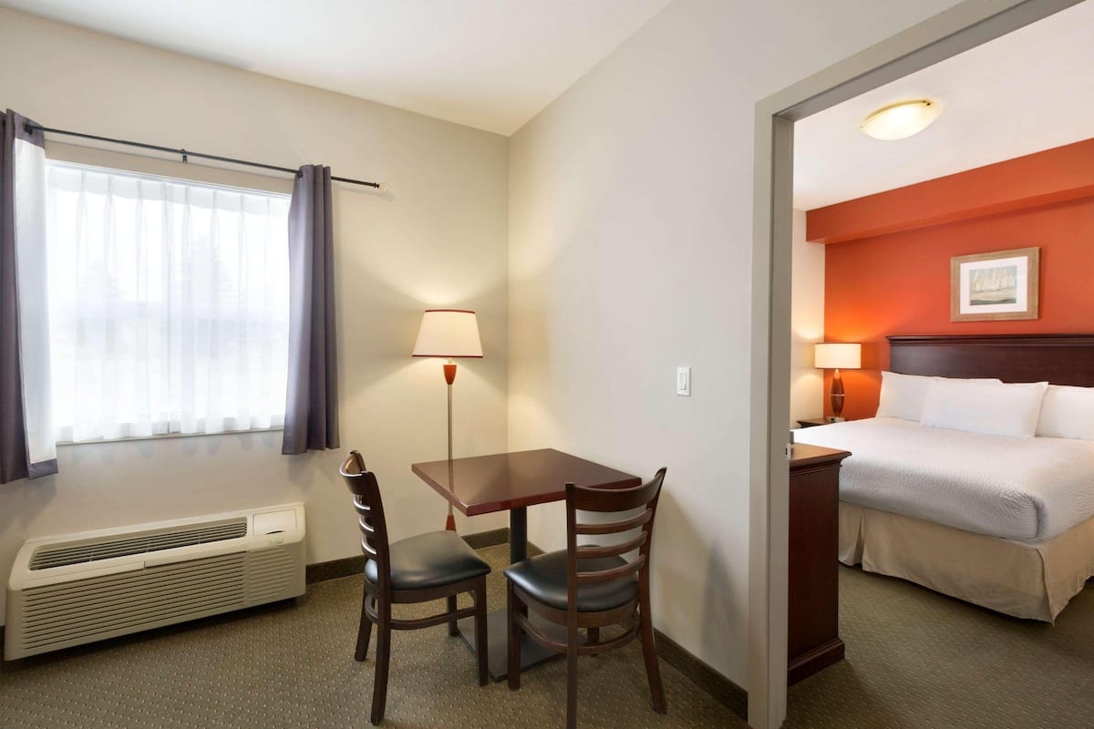 Een hotelkamer met een bed, een bureau met twee stoelen, een tafellamp, een staande lamp en een raam met gordijnen.