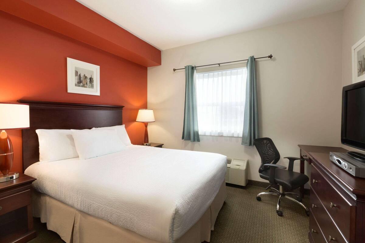 Hotelkamer met een groot bed, een bureau met een computer, een stoel, een televisie en een raam met gordijnen.