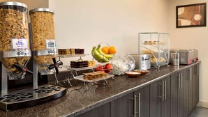 Un buffet proposant des distributeurs de céréales, un saladier de fruits et un espace dédié au café.
