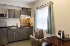 A compact kitchen with dark cabinets, a microwave, a coffee maker, and a small dining table with patterned chairs. - Travelodge by Wyndham Kindersley (Kindersley)