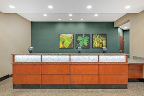 A reception desk with a green wall, three framed botanical prints, and two phones. - Drury Inn Pikes Peak Colorado Springs (Colorado Springs)