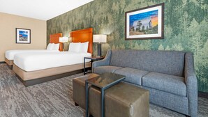 Ein Hotelzimmer mit Bett, Sofa, Couchtisch und Wand mit Walddruck.