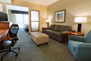 A hotel room with a desk, office chair, sofa, ottoman, and a bed with a window view. - Drury Inn Pikes Peak Colorado Springs (Colorado Springs)