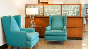 Un hall d’entrée avec deux fauteuils turquoise, une petite table avec une lampe et un comptoir d’accueil doté d’un panneau décoratif aux motifs géométriques.